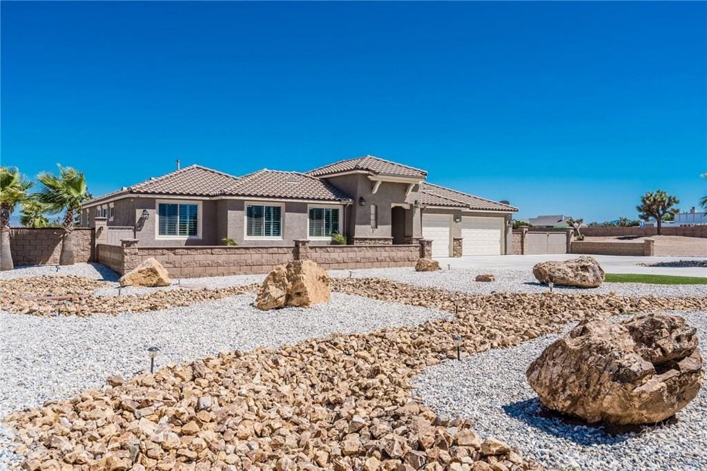 view of front of home with an attached garage, fence, a tiled roof, concrete driveway, and stucco siding