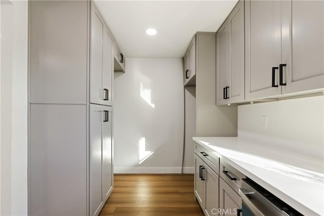 kitchen featuring baseboards, dishwasher, light wood-style flooring, light countertops, and recessed lighting