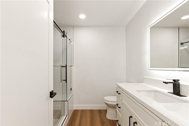 bathroom featuring baseboards, toilet, wood finished floors, a shower with shower door, and vanity