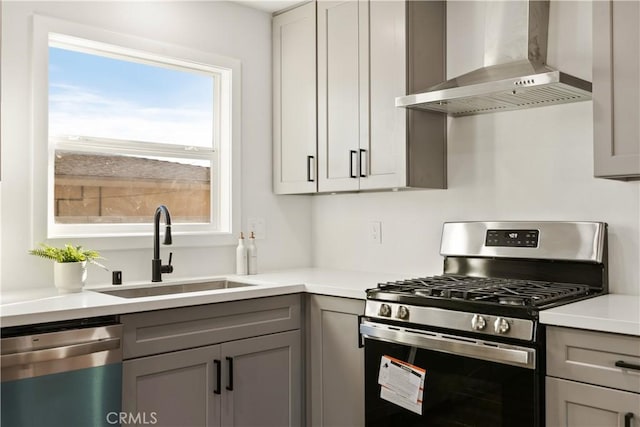 kitchen featuring wall chimney range hood, stainless steel appliances, a sink, and gray cabinetry