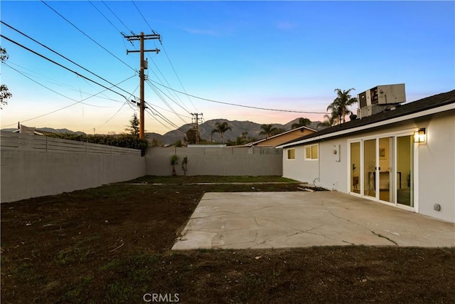 yard at dusk with a fenced backyard, cooling unit, and a patio