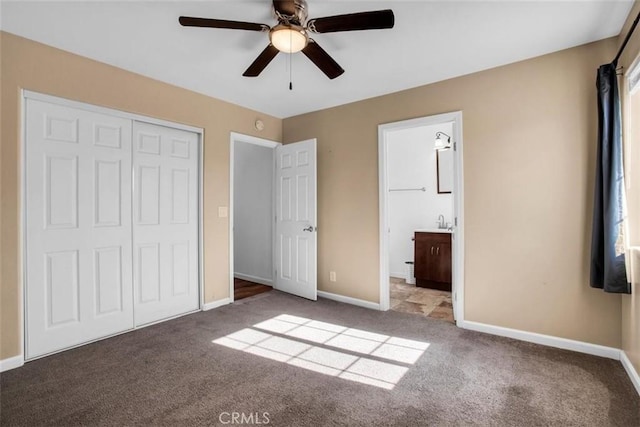 unfurnished bedroom with a closet, carpet flooring, ceiling fan, ensuite bath, and baseboards