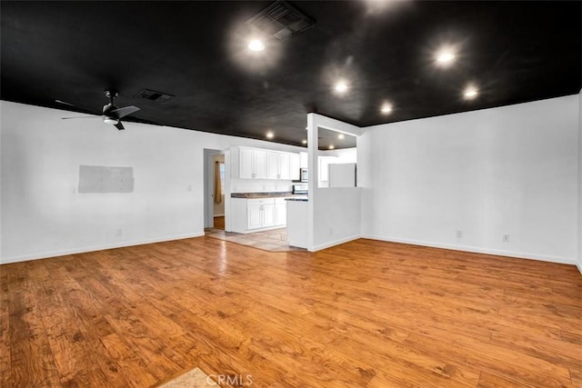 interior space with light wood-style flooring, visible vents, ceiling fan, and baseboards