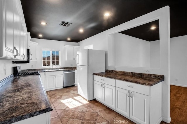 kitchen with dark countertops, visible vents, stainless steel dishwasher, stove, and freestanding refrigerator