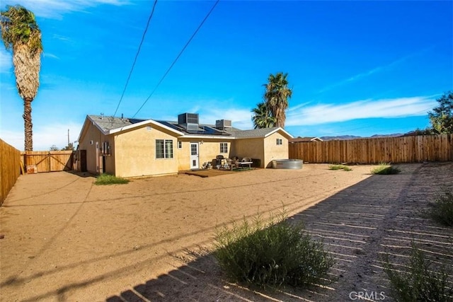 rear view of property featuring solar panels, a fenced backyard, and stucco siding