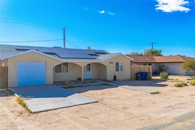 view of front of home with driveway, a garage, fence, roof mounted solar panels, and stucco siding