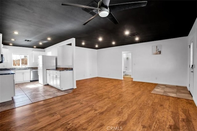 unfurnished living room featuring visible vents, light wood-style floors, a ceiling fan, a sink, and baseboards