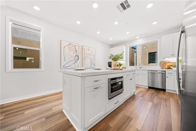 kitchen featuring light wood-style flooring, stainless steel appliances, visible vents, white cabinets, and light countertops