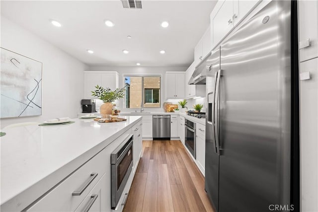 kitchen with stainless steel appliances, visible vents, white cabinetry, light countertops, and light wood-type flooring