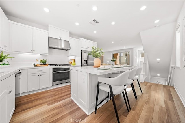 kitchen featuring stainless steel appliances, visible vents, a kitchen island, under cabinet range hood, and a kitchen breakfast bar