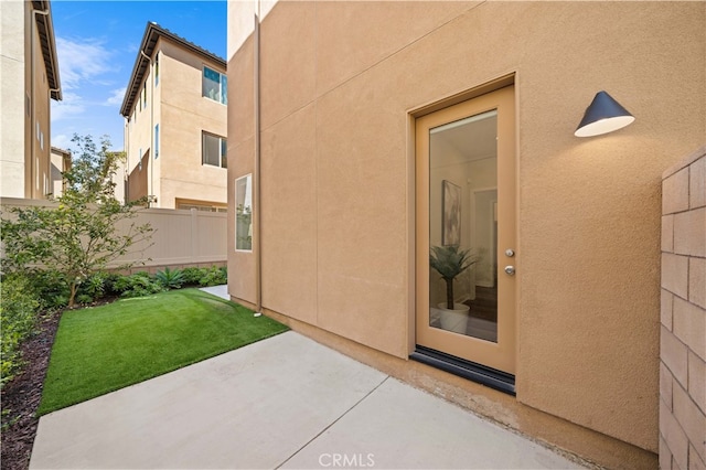 entrance to property featuring a patio area, fence, and stucco siding