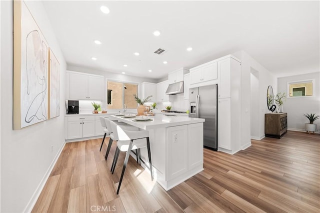 kitchen with light wood finished floors, stainless steel fridge, a center island, under cabinet range hood, and white cabinetry