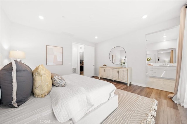 bedroom featuring light wood-type flooring, a sink, ensuite bathroom, and recessed lighting