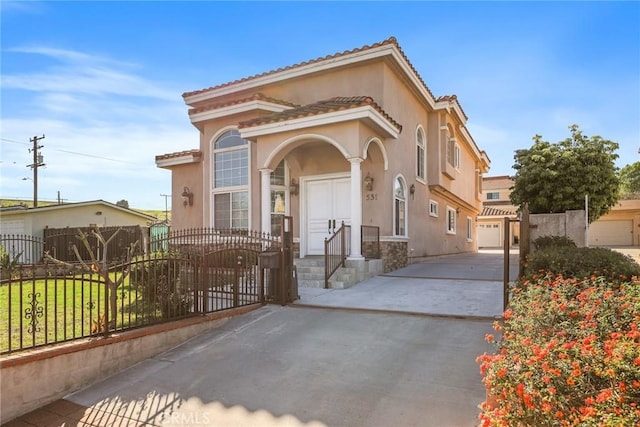 mediterranean / spanish-style house featuring a garage, a fenced front yard, and stucco siding
