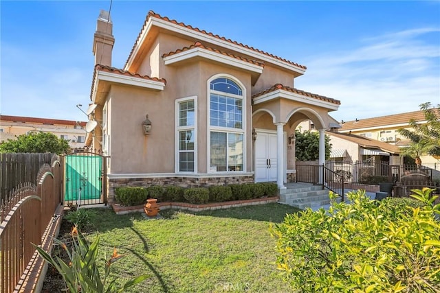 mediterranean / spanish-style home featuring stucco siding, a front yard, a gate, fence, and stone siding