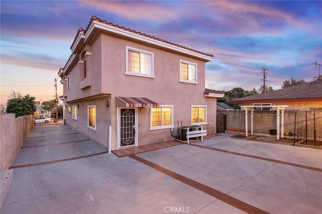 back of house at dusk with a patio area, a tiled roof, fence, and stucco siding
