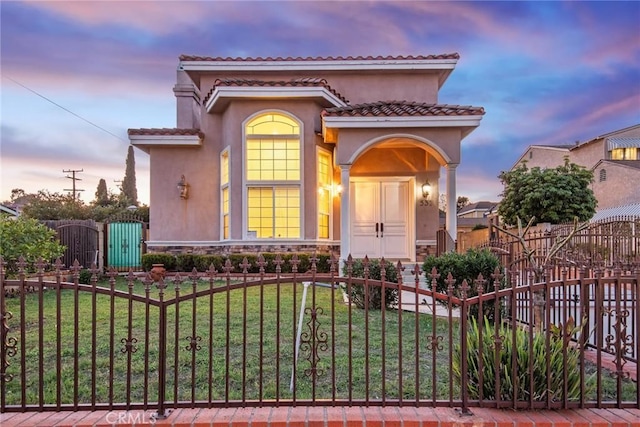 mediterranean / spanish house featuring a fenced front yard, stone siding, a gate, stucco siding, and a front lawn