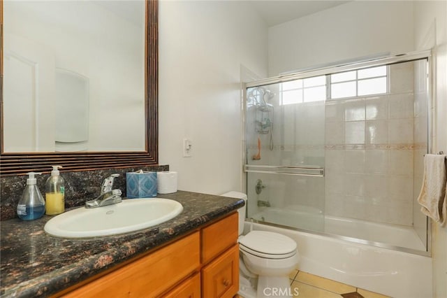bathroom featuring toilet, combined bath / shower with glass door, tile patterned flooring, and vanity
