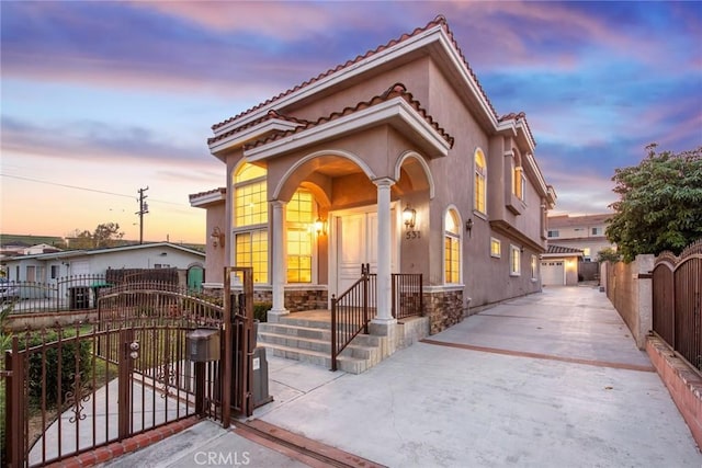 mediterranean / spanish home featuring a fenced front yard, a garage, a tile roof, a gate, and stucco siding