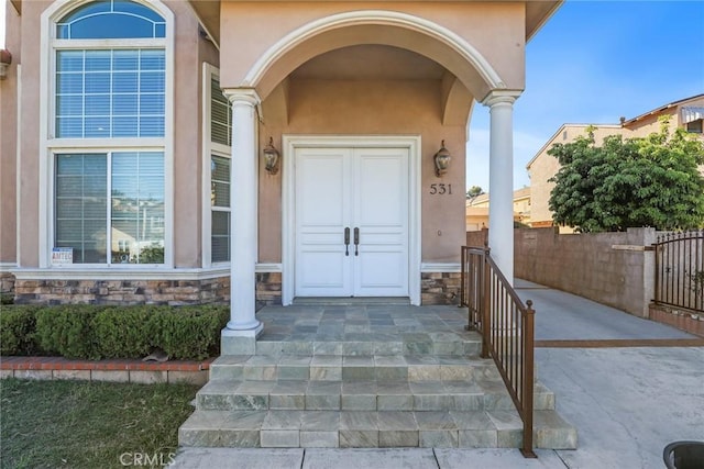 entrance to property featuring stone siding, fence, and stucco siding