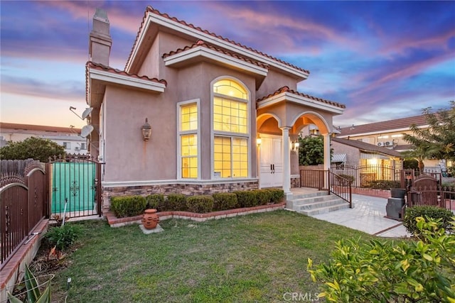rear view of house featuring stone siding, a gate, fence, a yard, and stucco siding