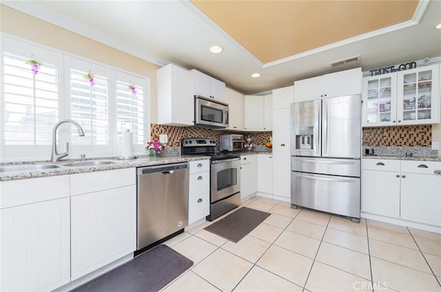 kitchen with light tile patterned floors, stainless steel appliances, backsplash, glass insert cabinets, and a sink