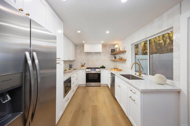 kitchen featuring light stone counters, stainless steel appliances, a sink, white cabinets, and light wood-type flooring