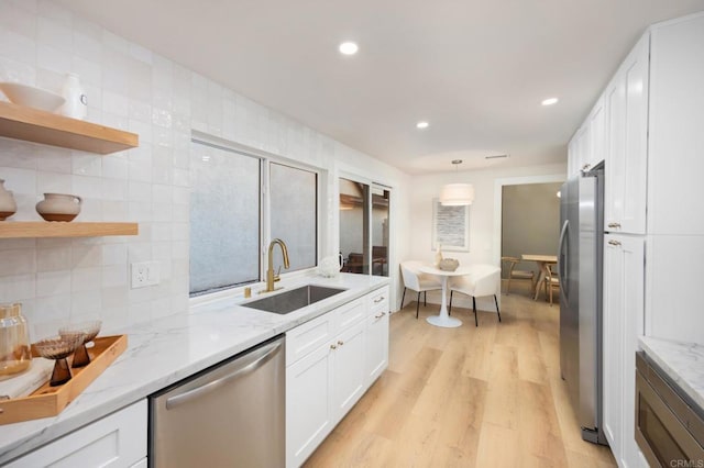 kitchen with light stone counters, stainless steel appliances, light wood-style floors, white cabinetry, and a sink