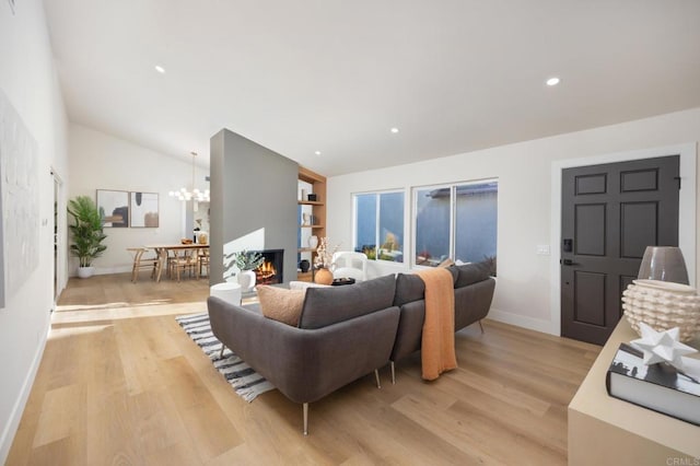 living room featuring a warm lit fireplace, lofted ceiling, light wood-style flooring, recessed lighting, and a notable chandelier