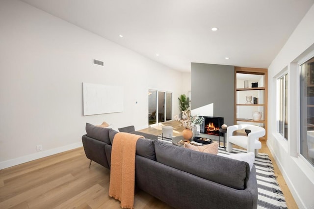 living room featuring recessed lighting, visible vents, baseboards, a lit fireplace, and light wood finished floors