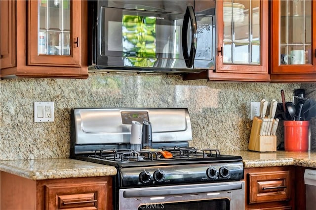 kitchen featuring stainless steel gas range, black microwave, brown cabinets, and tasteful backsplash