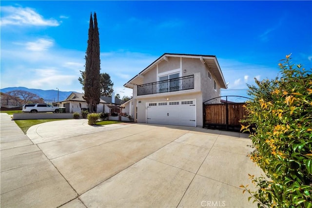 view of front of home featuring a balcony, a garage, fence, driveway, and stucco siding