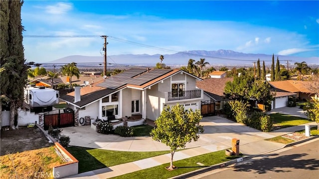 view of front of home featuring a balcony, a mountain view, solar panels, fence, and driveway