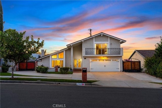 view of front of home with an attached garage, a balcony, fence, driveway, and a gate