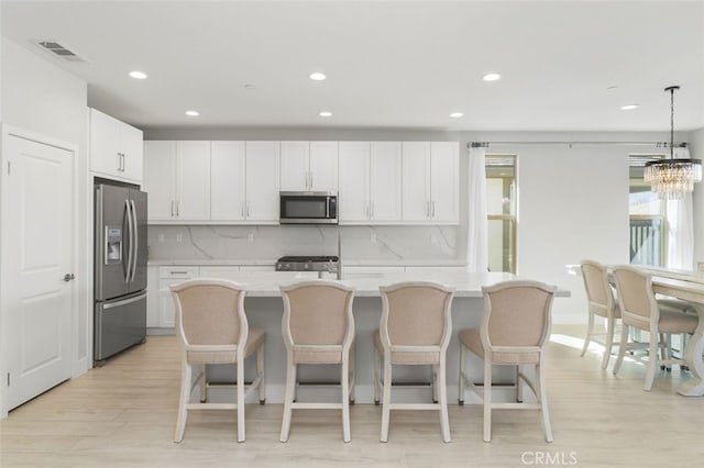 kitchen with light wood-style flooring, visible vents, white cabinetry, appliances with stainless steel finishes, and a center island with sink