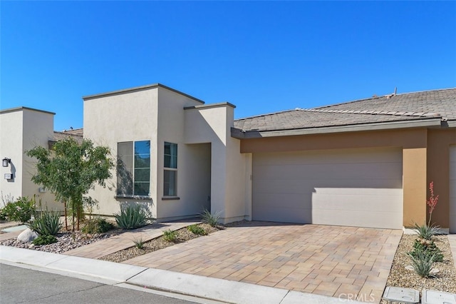 contemporary home with an attached garage, decorative driveway, and stucco siding