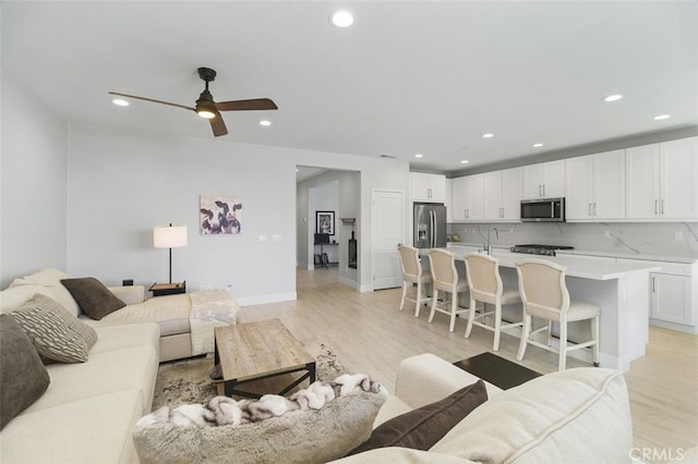 living area featuring light wood-style flooring, baseboards, a ceiling fan, and recessed lighting