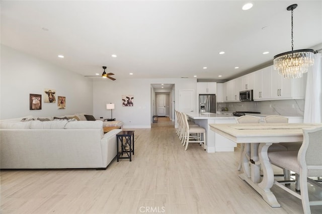 living room featuring light wood-style floors, baseboards, ceiling fan with notable chandelier, and recessed lighting