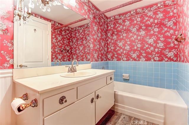 bathroom with wallpapered walls, wainscoting, a bathing tub, wood finished floors, and vanity