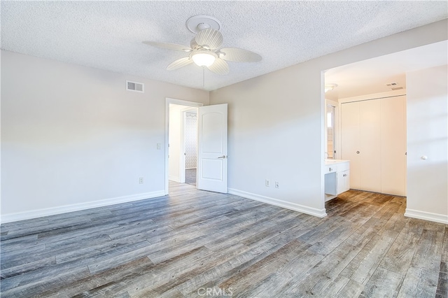 unfurnished bedroom featuring baseboards, a textured ceiling, visible vents, and wood finished floors