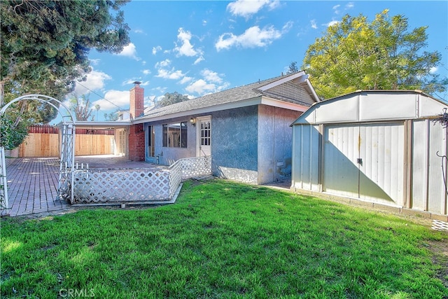 back of house with an outbuilding, stucco siding, a storage unit, a lawn, and fence