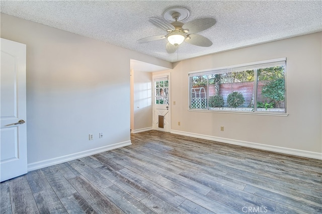 empty room with a textured ceiling, ceiling fan, wood finished floors, and baseboards