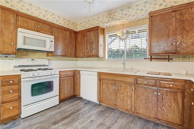 kitchen featuring a sink, white appliances, brown cabinetry, and wallpapered walls