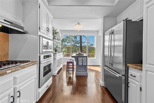 kitchen with dark wood finished floors, appliances with stainless steel finishes, white cabinets, under cabinet range hood, and baseboards