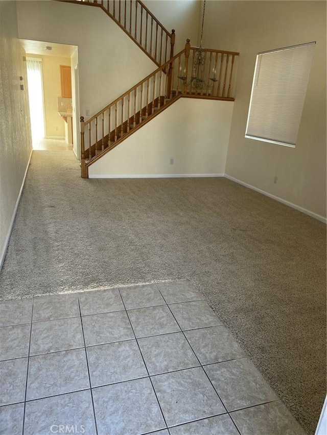 unfurnished living room featuring carpet, stairs, baseboards, and tile patterned floors