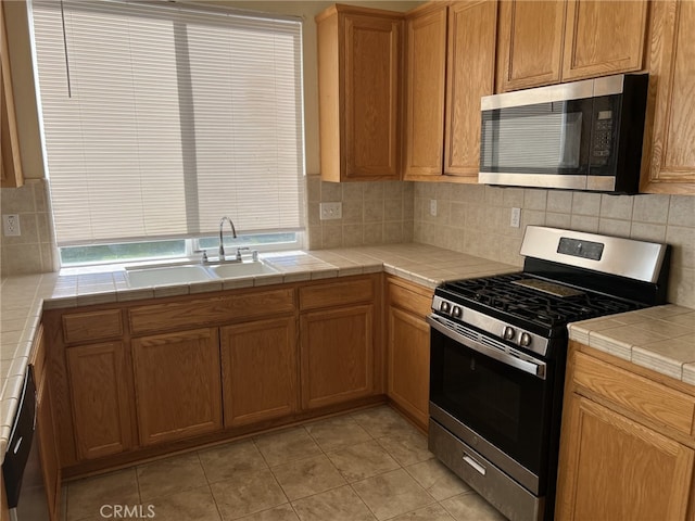 kitchen featuring light tile patterned floors, decorative backsplash, tile countertops, stainless steel appliances, and a sink