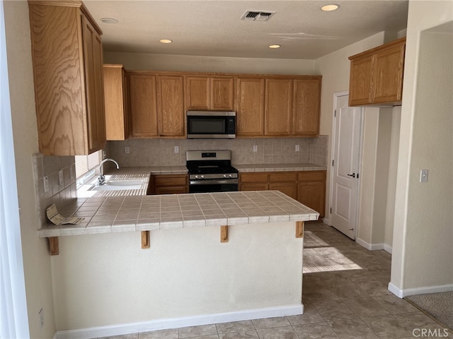 kitchen with tile countertops, stainless steel appliances, a peninsula, a sink, and visible vents