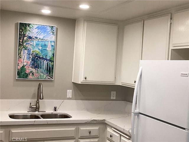 kitchen featuring light stone counters, freestanding refrigerator, white cabinetry, a sink, and recessed lighting