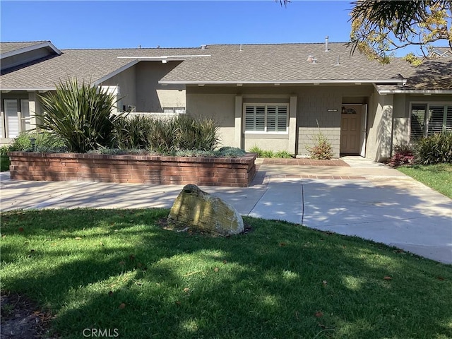 ranch-style house featuring roof with shingles, a front lawn, and stucco siding