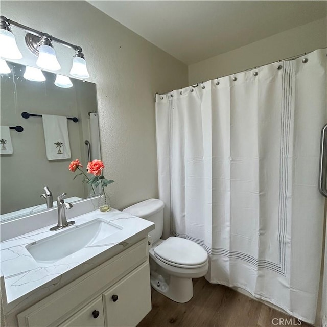 bathroom with a textured wall, toilet, a shower with shower curtain, wood finished floors, and vanity